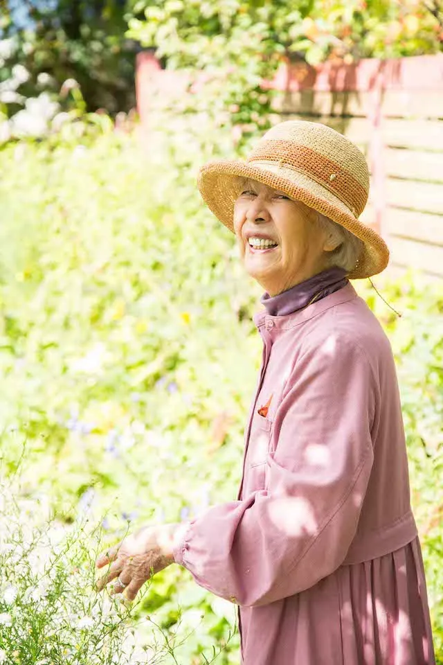 ローズカラーのワンピースにお気に入りの帽子を組み合わせて、庭を散歩する92歳の祖母。